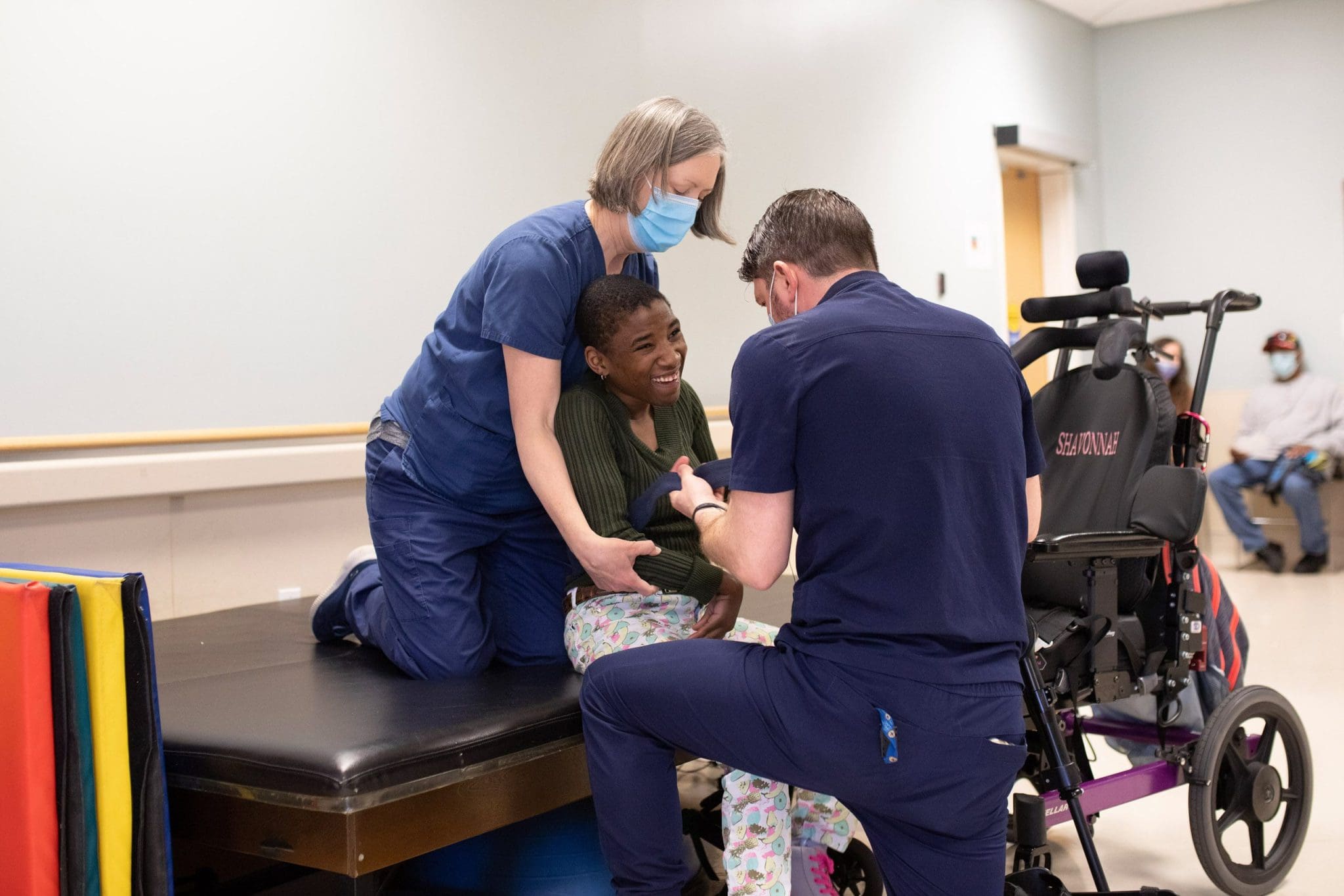 Two physical therapists assist a patient with intellectual and developmental disabilities (IDD) in preparing for walking exercises, focusing on mobility, strength, and independence in a supportive rehabilitation setting.